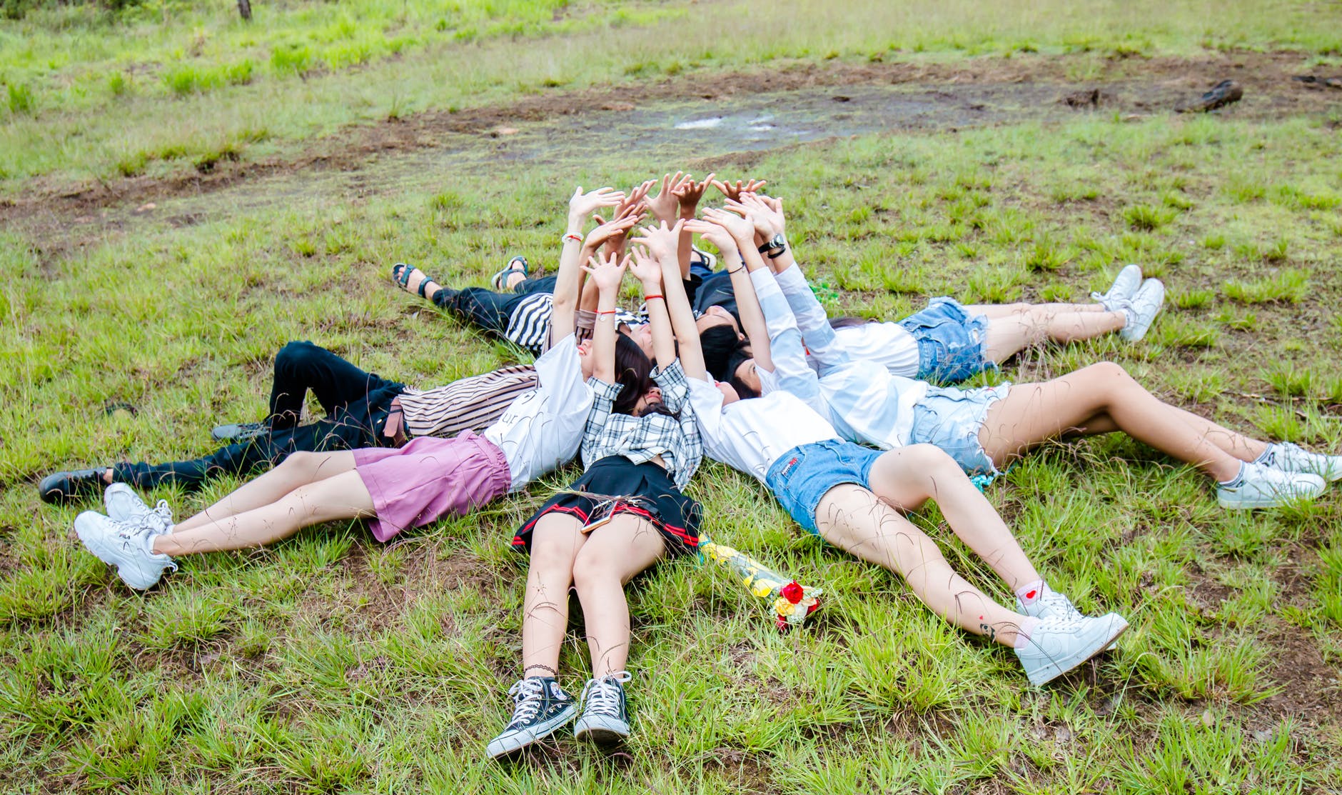group of friends form in circle while lying on the grass while hands on top